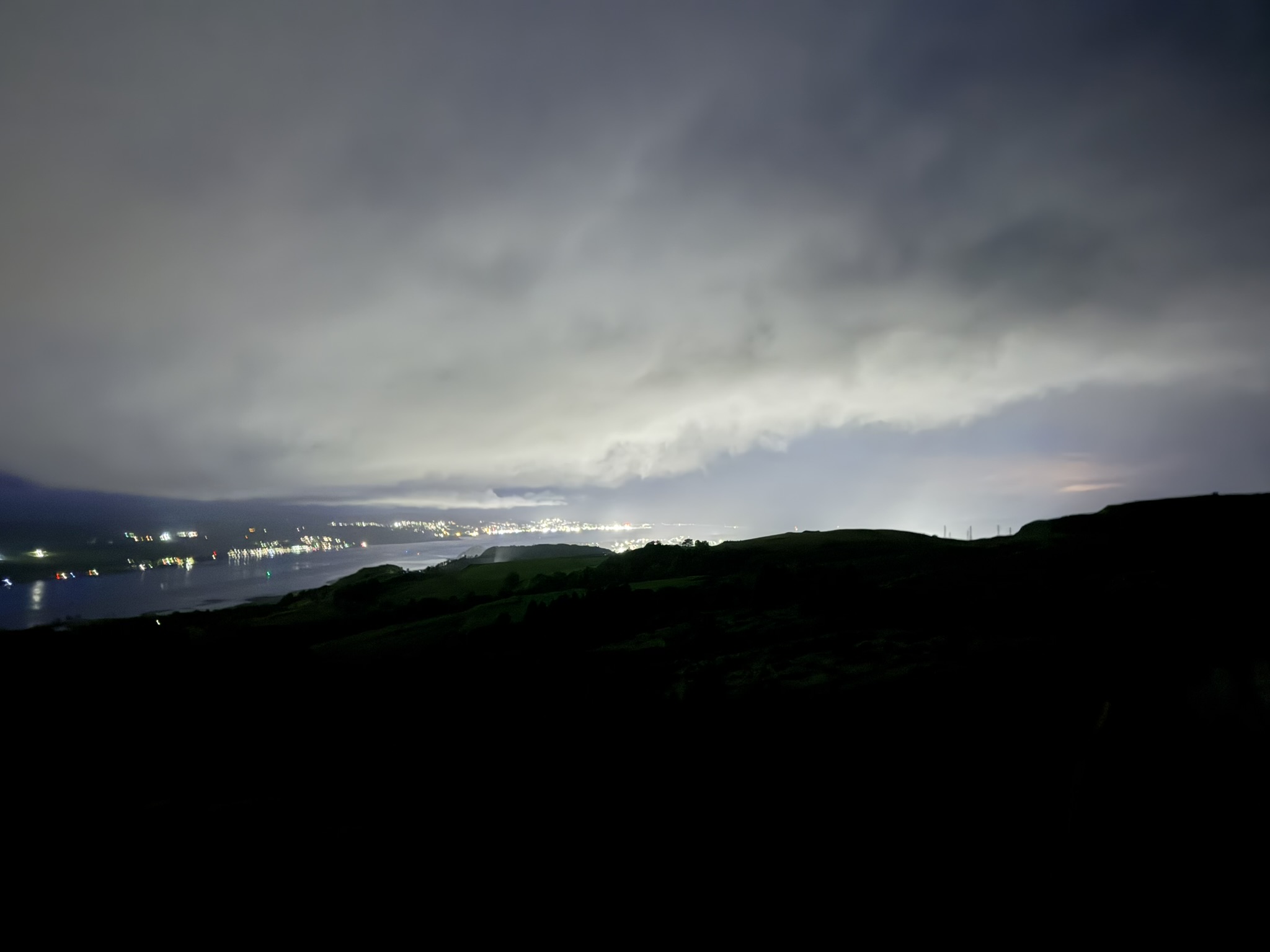 Night view over the Clyde from a hillside near Dumbarton, city lights soft under thick cloud