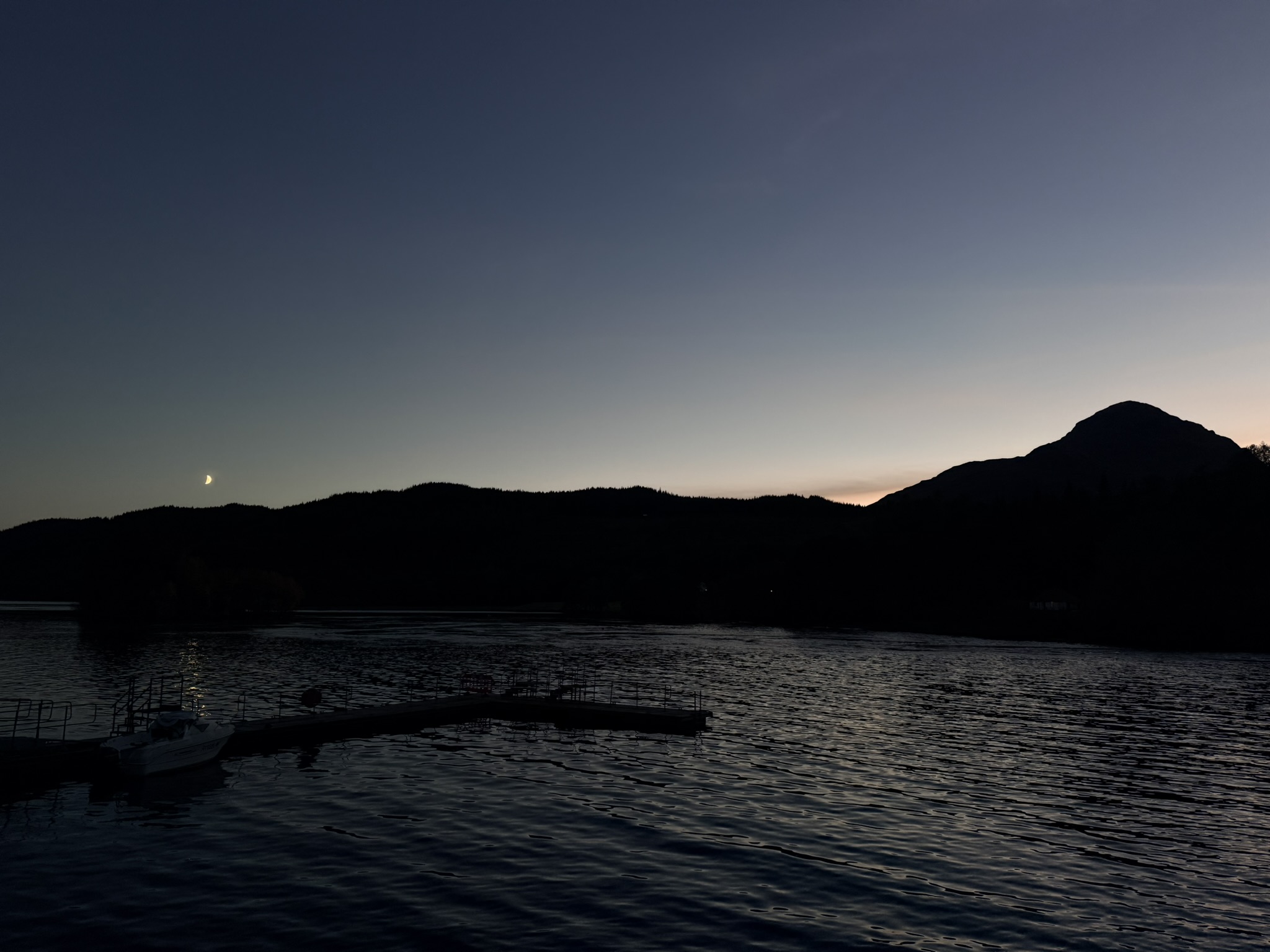 Wide dusk view over Loch Lomond, the moon low and the higher hill to its right.