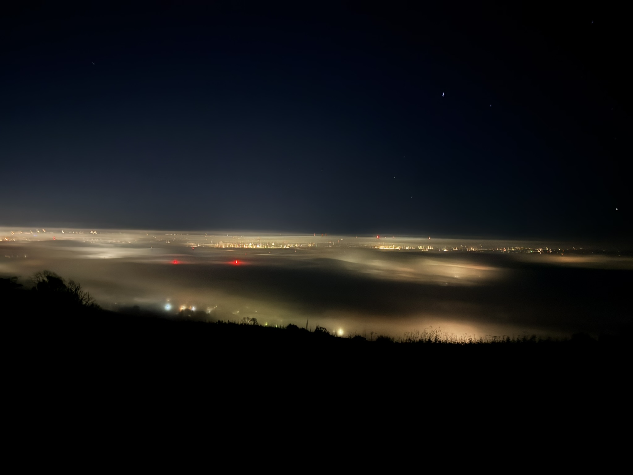 A cloud-filled valley with town lights glowing through the cloud under a clear dark sky