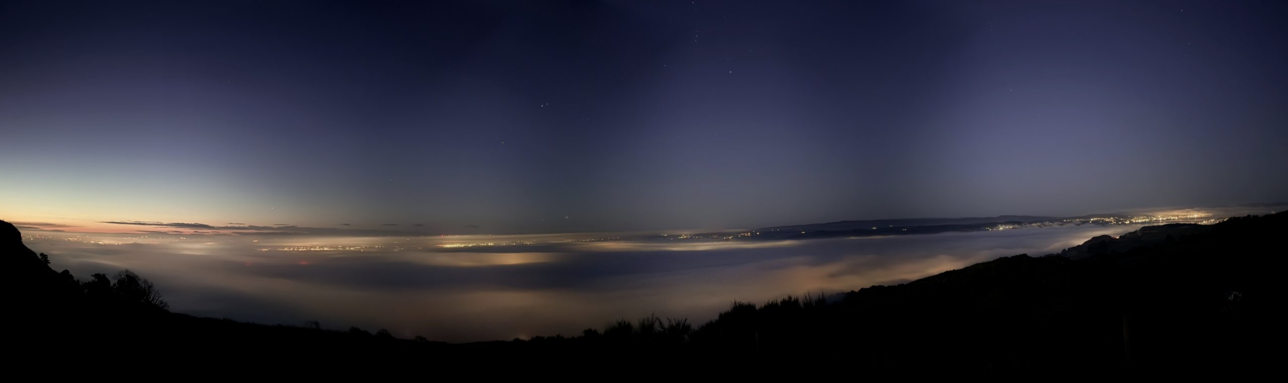 Panorama of the cloud-filled valley at dawn, from the sunset glow on the left to the starry sky on the right